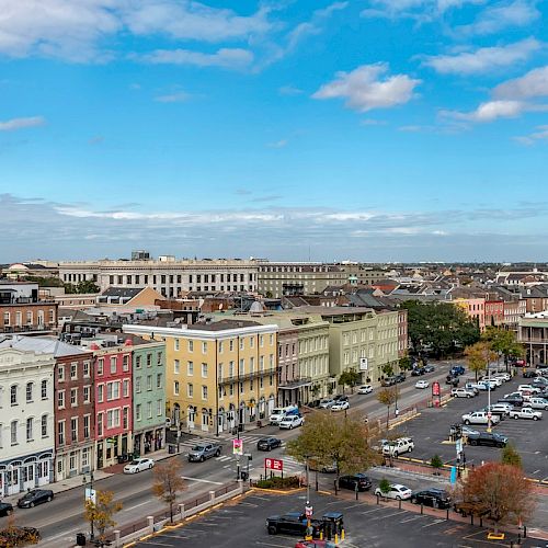 The image shows a cityscape with historical buildings, colorful facades, a parking lot, and clear skies.