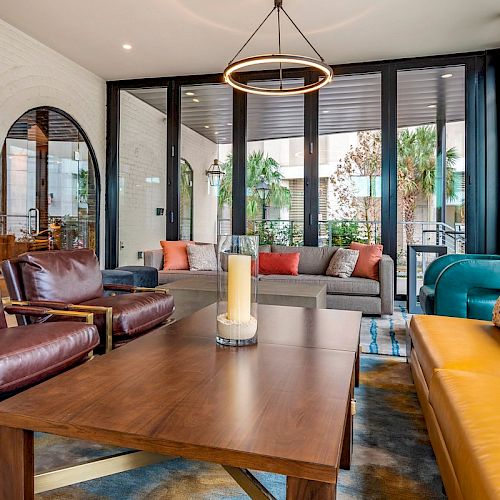 A modern living room with leather chairs, a wooden coffee table, a yellow sofa, and large windows overlooking the outdoors.