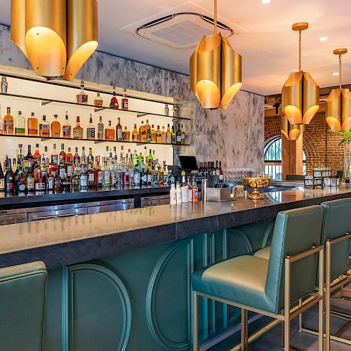 Elegant bar with modern gold lighting, a marble backdrop, and well-stocked shelves. High stools line the sleek counter under a warm ambiance.