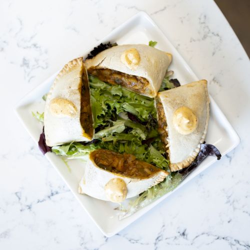 A plate holds four pita wraps filled with leafy greens, herbs, and a protein, garnished with small dollops of sauce on top.