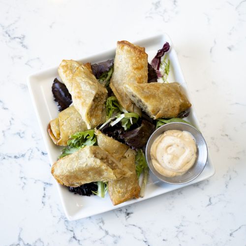Hexagonal plate with golden-brown fried pastries or quesadillas, fresh greens, and a small cup of creamy dipping sauce on a marble table.