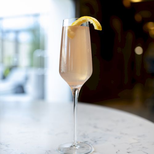 A cocktail in a flute glass with a lemon twist garnish, placed on a marble table.