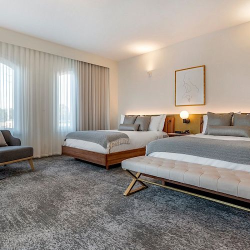 A modern hotel room with two neatly made beds, a chair, large windows with sheer curtains, a floor lamp, and minimalistic decor, in soft neutral tones.