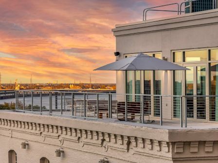 A rooftop terrace with a seating area and umbrella overlooks a scenic view at sunset.