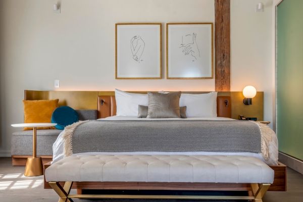 A modern bedroom features a neatly made bed with gray and white bedding, abstract wall art, and a cushioned bench at the foot of the bed.