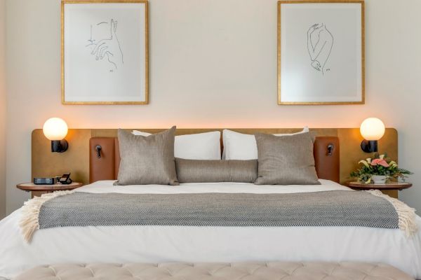 A neatly made bed with cushions and a throw, flanked by nightstands with lamps, and two framed minimalist artworks above the headboard.