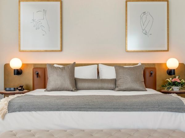 A neatly made bed with cushions and a throw, flanked by nightstands with lamps, and two framed minimalist artworks above the headboard.