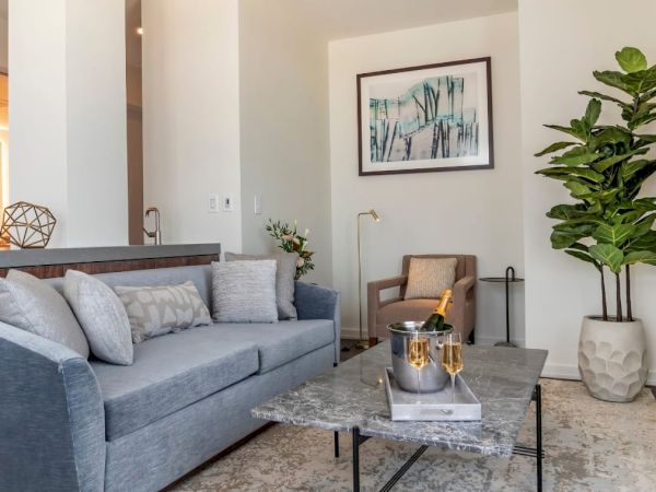 A modern living room with a grey couch, coffee table, armchair, plant, wall art, and decor items, featuring neutral tones and a cozy ambiance.