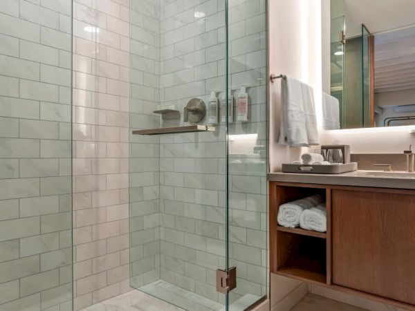 A modern bathroom featuring a glass shower enclosure, tiled walls, a vanity unit with folded towels, a mirror, and a sink with a countertop.
