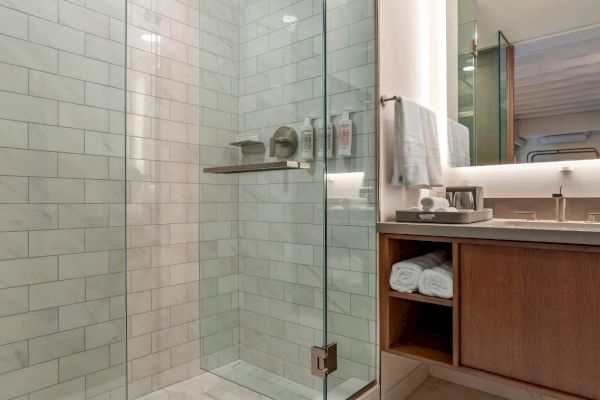 A modern bathroom featuring a glass shower enclosure, tiled walls, a vanity unit with folded towels, a mirror, and a sink with a countertop.