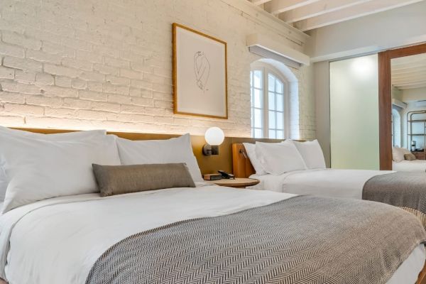 A cozy bedroom with two double beds, white brick walls, modern decor, wooden accents, and ambient lighting seen in the image. The sentence ends.