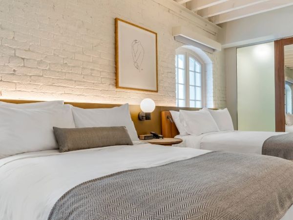 A cozy bedroom with two double beds, white brick walls, modern decor, wooden accents, and ambient lighting seen in the image. The sentence ends.