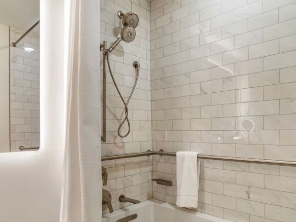 A bathroom with white subway tile walls, a showerhead, a bathtub with grab bars, and a towel hanging over one of the bars.