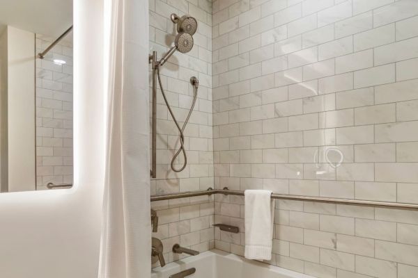 A bathroom with white subway tile walls, a showerhead, a bathtub with grab bars, and a towel hanging over one of the bars.