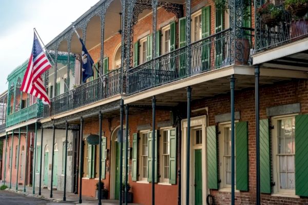 A street scene with historic buildings, featuring balconies, colorful shutters, and U.S. flags displayed prominently.