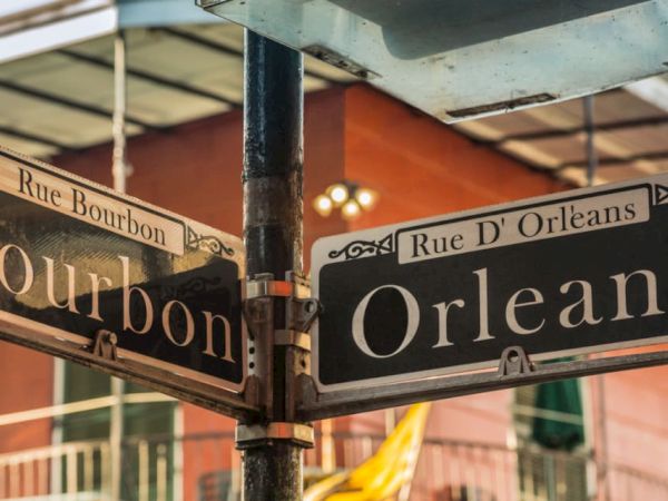 A street sign at the corner of Rue Bourbon and Rue D'Orléans in a vibrant area, with buildings in the background.