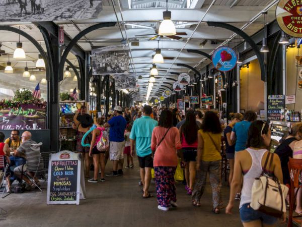 A bustling indoor market with numerous people walking and dining, various stalls selling goods, and signage hanging from the ceiling.