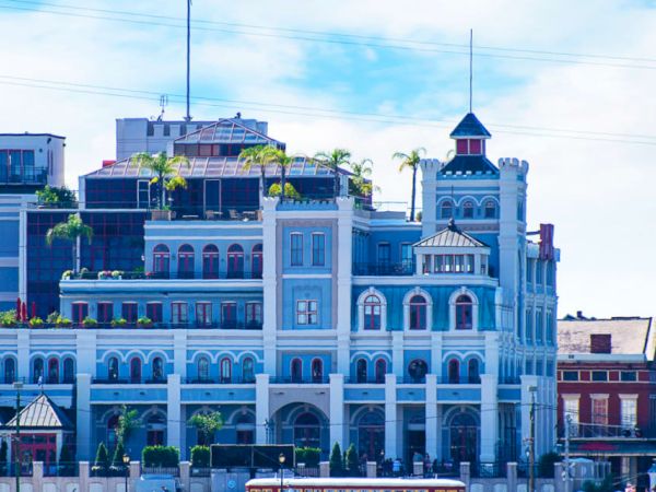 A multi-story building with an ornate design and a blue facade, featuring balconies, arched windows, and rooftop greenery.