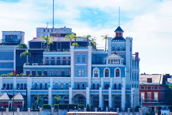 A multi-story building with an ornate design and a blue facade, featuring balconies, arched windows, and rooftop greenery.