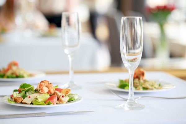 Three plates of salads are set on a white tablecloth with empty wine glasses, ready for a meal.