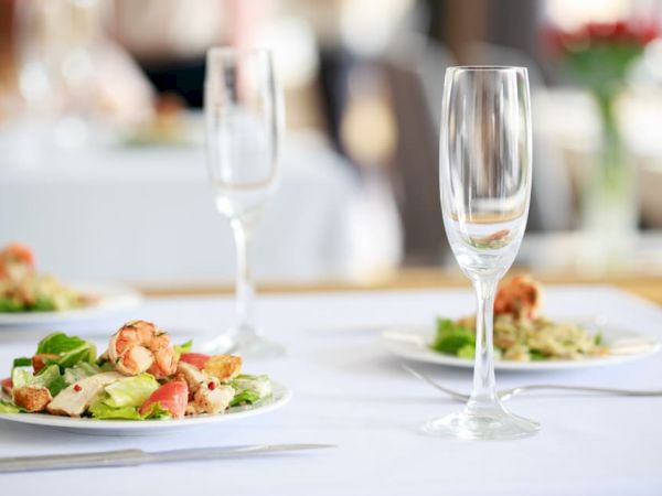 Three plates of salads are set on a white tablecloth with empty wine glasses, ready for a meal.