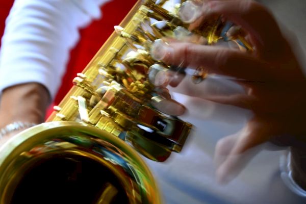 A close-up of a person playing a saxophone, with a blurred motion effect on the fingers on the instrument.