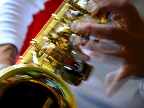 A close-up of a person playing a saxophone, with a blurred motion effect on the fingers on the instrument.