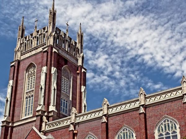 The image showcases a red-brick Gothic-style church with ornate windows and a tall tower against a blue sky with scattered clouds.