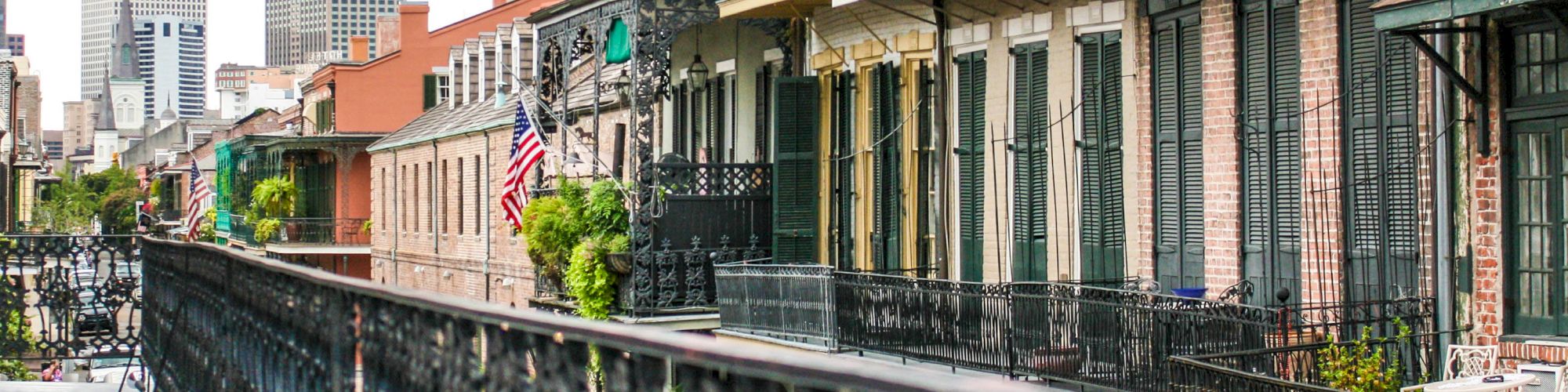 This image shows a street view with historic buildings featuring wrought-iron balconies and an American flag; skyscrapers are visible in the background.