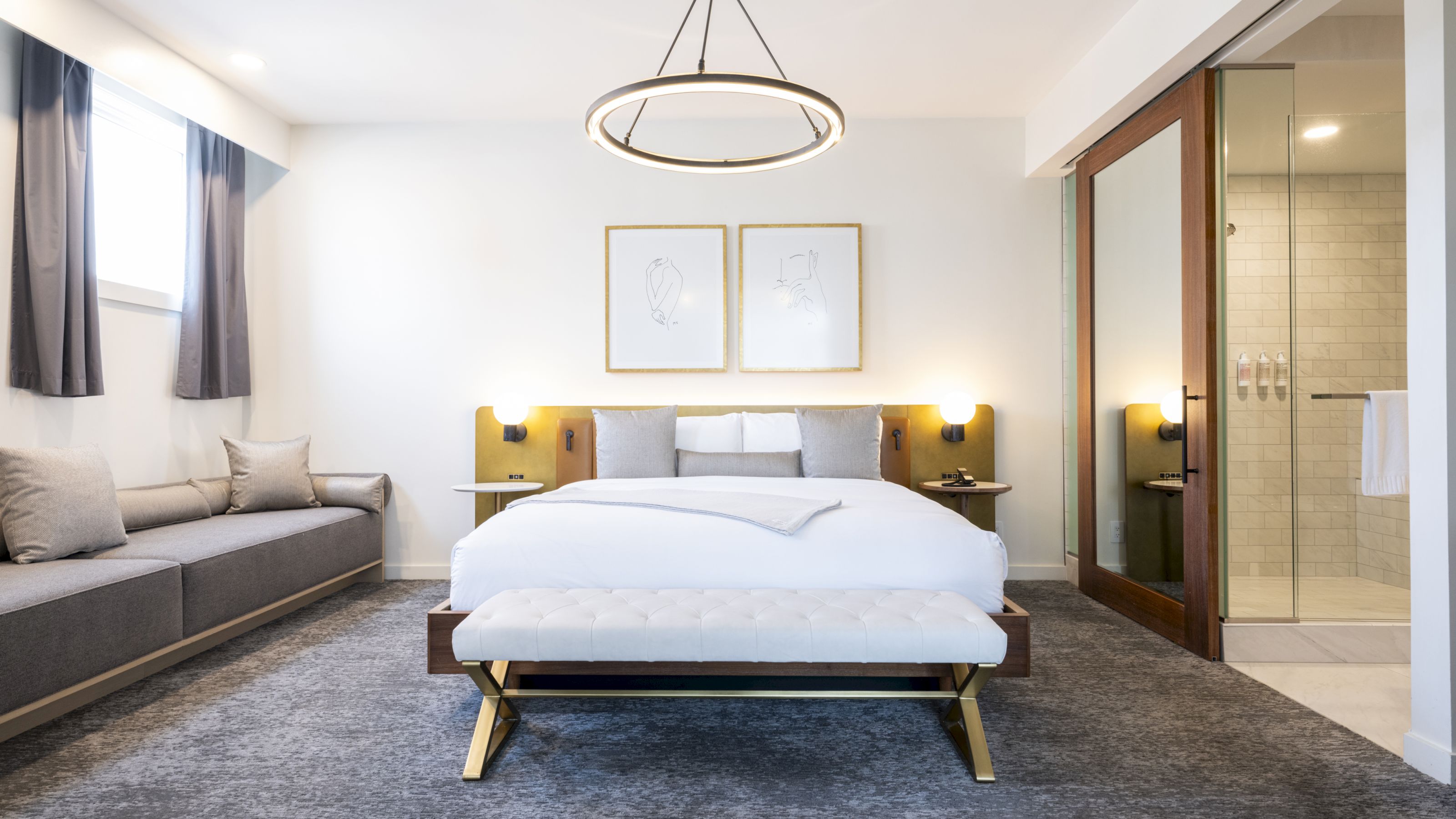A wide view of a hotel room with a king-sized bed, a gray couch, and a glass-enclosed shower.