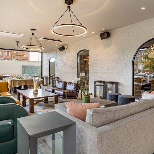 A modern living space with a mix of seating, including a gray sofa, green chairs, and a dining table, set in a room with arched doorways and pendant lights.