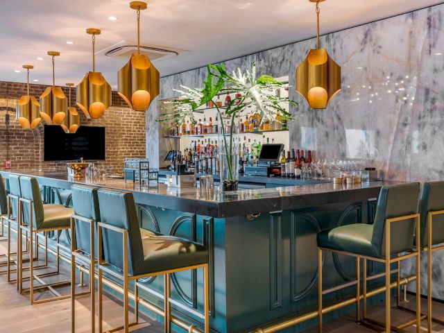 A bar with a marble wall, gold light fixtures, and several bar stools.