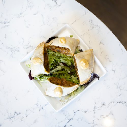 The image shows a white square plate with triangular pieces of stuffed bread and some greens on a marble surface.