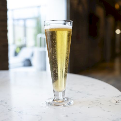 A tall glass filled with a light, bubbly beverage is placed on a marble table in a modern, softly-lit setting.