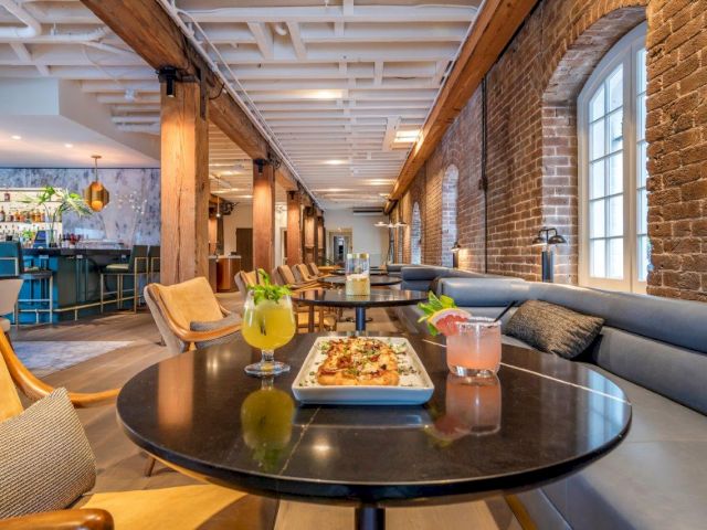 A stylish hotel lounge with a black table, gray booth seating, and a plate of food and drinks.