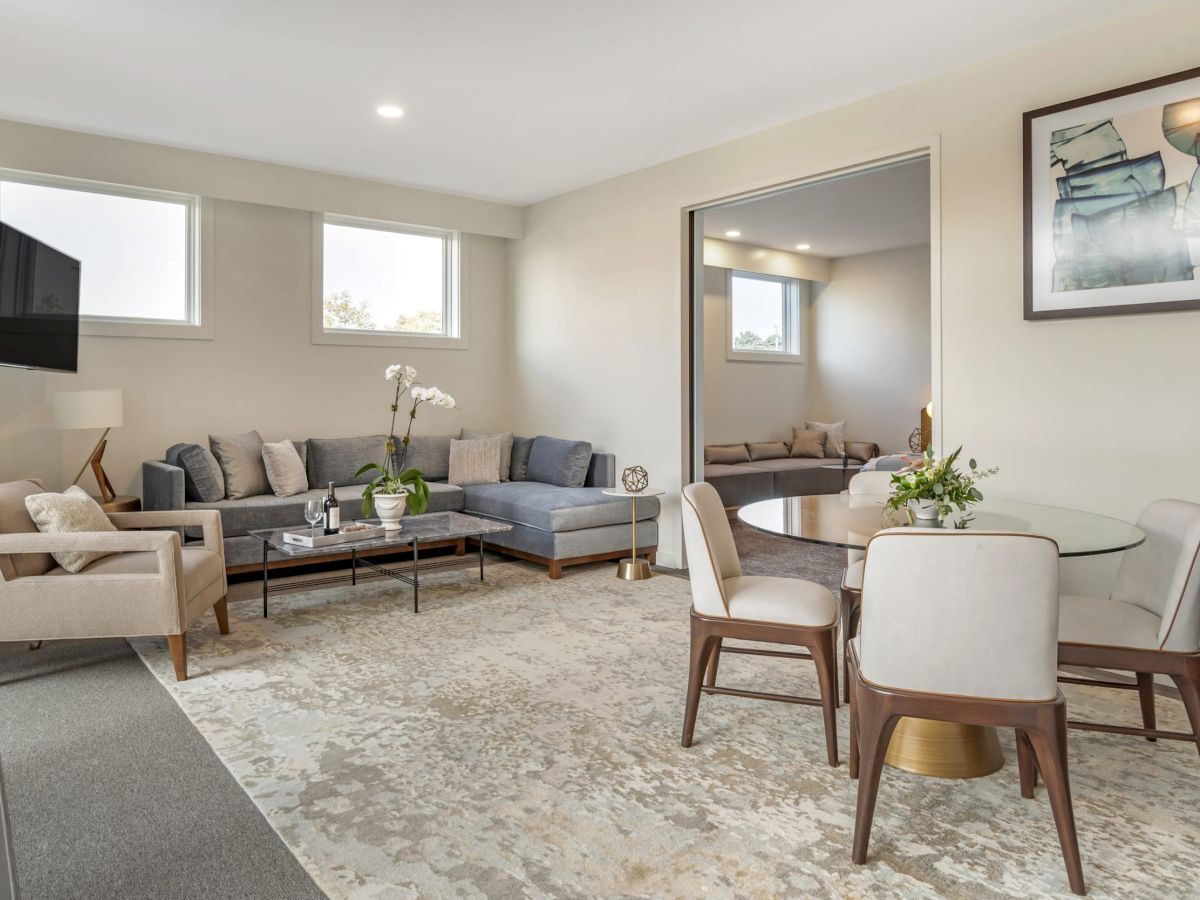 A modern living and dining room with a sectional sofa, armchair, wall-mounted TV, dining table with chairs, and a large rug.