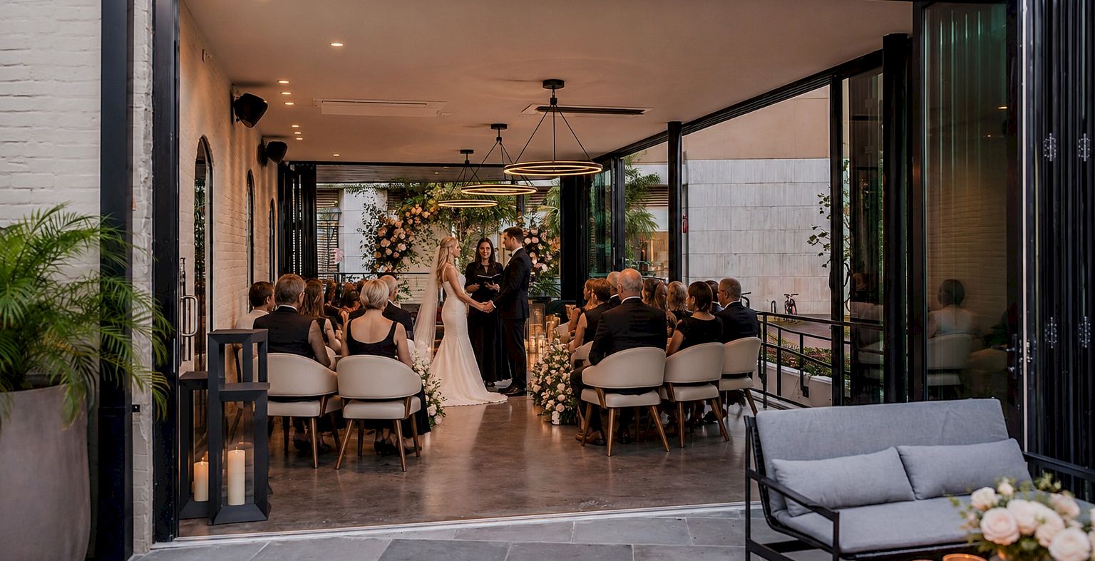 An elegant outdoor wedding ceremony with a couple and guests seated in rows under hanging lights and floral decor.