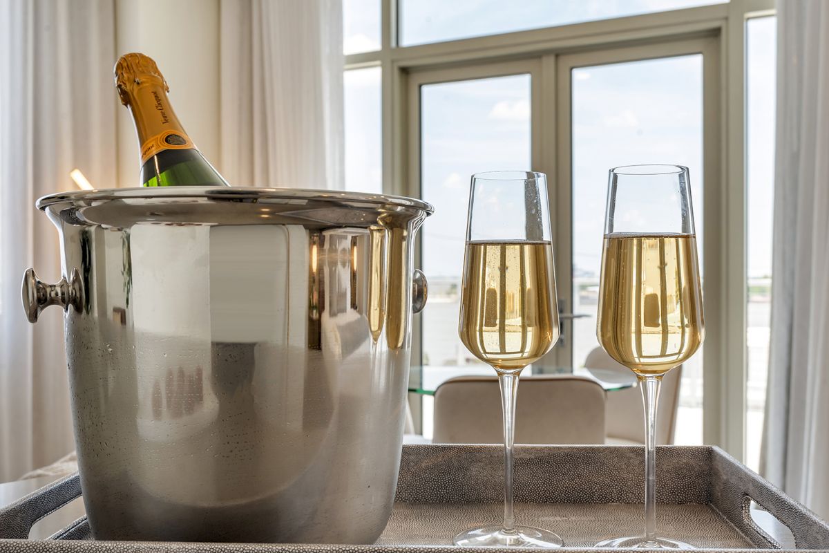 A champagne bottle chills in a metal ice bucket beside two filled flutes on a tray, likely ready to toast.