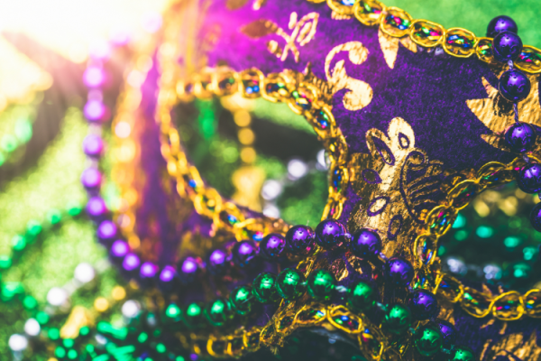 The image features a decorative purple and gold masquerade mask adorned with intricate designs, along with green and purple beads, likely for a carnival or Mardi Gras.