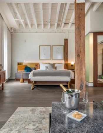 A modern bedroom features a bed, TV, wooden accents, and flowers on a table. An ice bucket and cookies enhance the cozy ambiance.