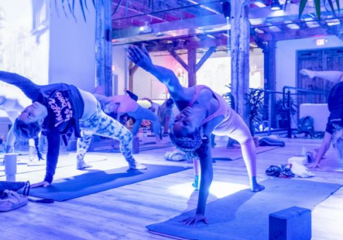 People doing yoga poses on mats in an indoor studio with blocks, under wooden beams and mirrored reflections, together.