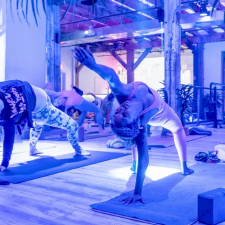 People doing yoga poses on mats in an indoor studio with blocks, under wooden beams and mirrored reflections, together.