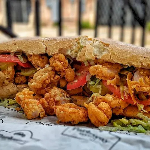 A crunchy fried-chicken sandwich with breaded bites, lettuce and tomato piled in a baguette, ready to eat.