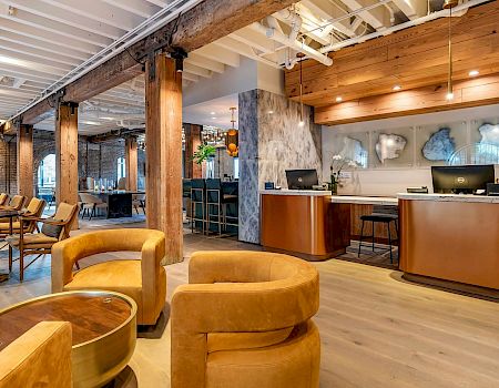 A stylish hotel lobby with warm wood tones, curved mustard sofas, wooden columns, a reception desk, and a cozy seating area.