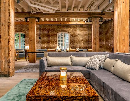 A stylish, industrial-style living area with a large gray sectional, wooden columns, brick walls, and a glossy brown coffee table, in a cozy loft.