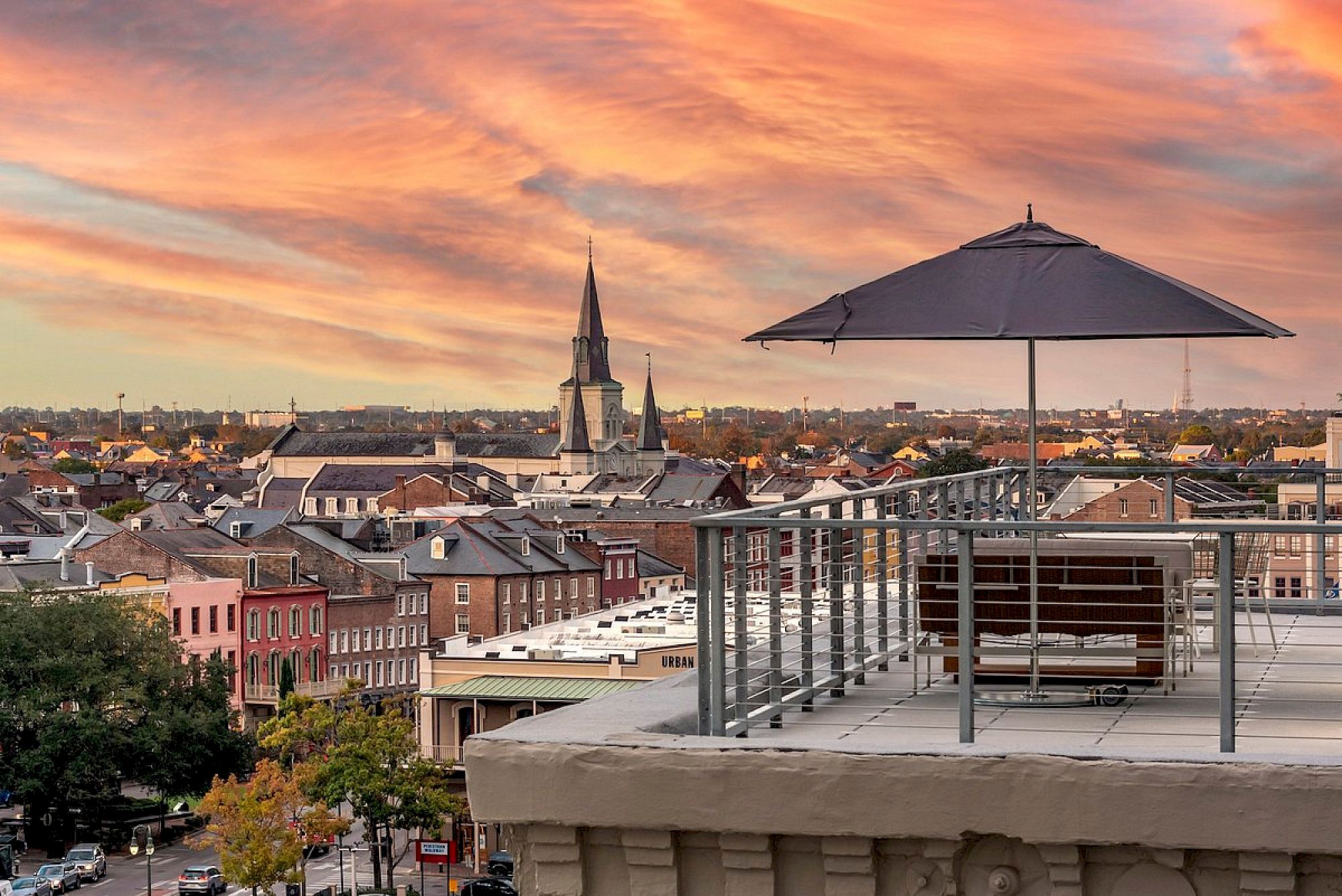 A rooftop terrace with a table, umbrella, and chair overlooking a colorful townscape at sunset.