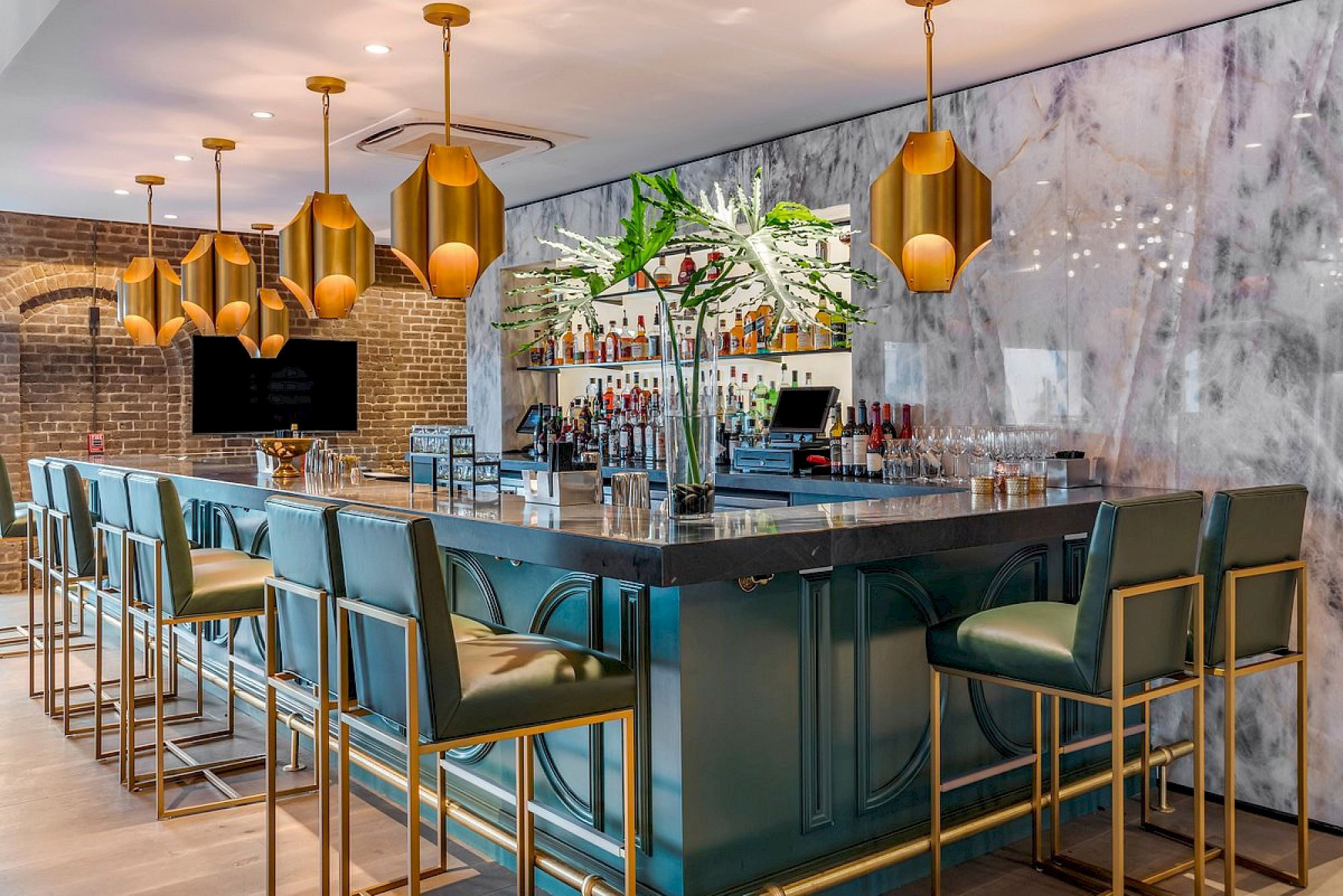 A stylish bar with teal counters, gold bar stools, marble walls, and gold pendant lights. Top it at 140 characters, always ending the sentence.