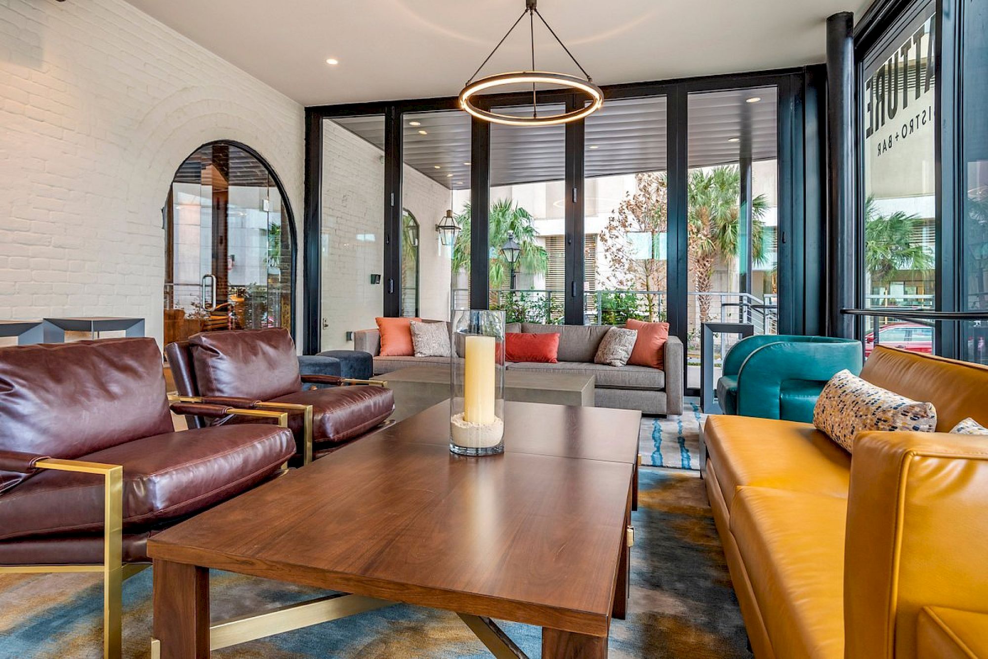 A bright, modern lounge with leather chairs, a wooden coffee table, colorful cushions, and large glass doors opening to a patio, creating a stylish, inviting space.