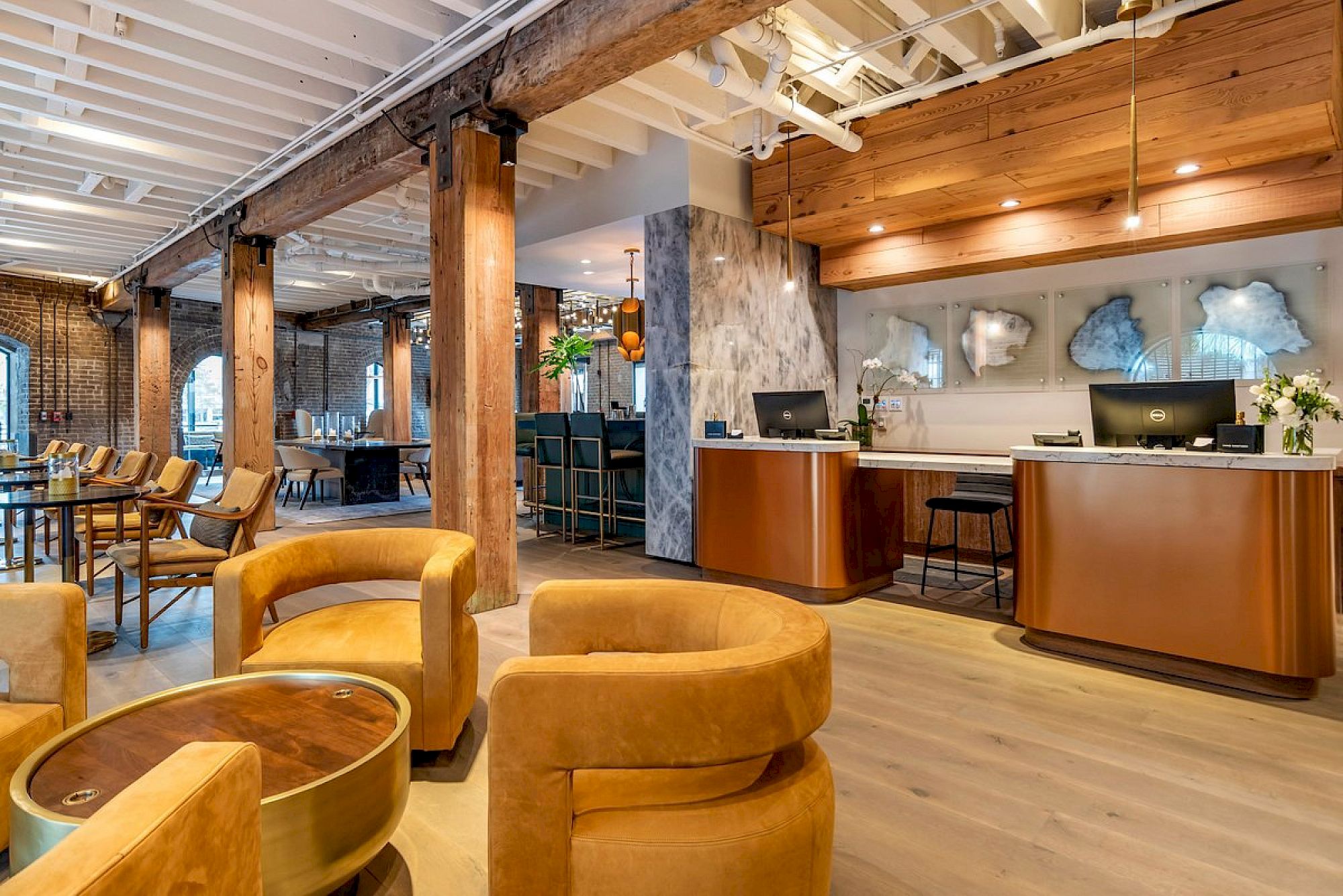 A stylish hotel lobby with warm wood tones, curved mustard sofas, a reception desk, and stone accents beneath exposed beams, welcoming and modern.