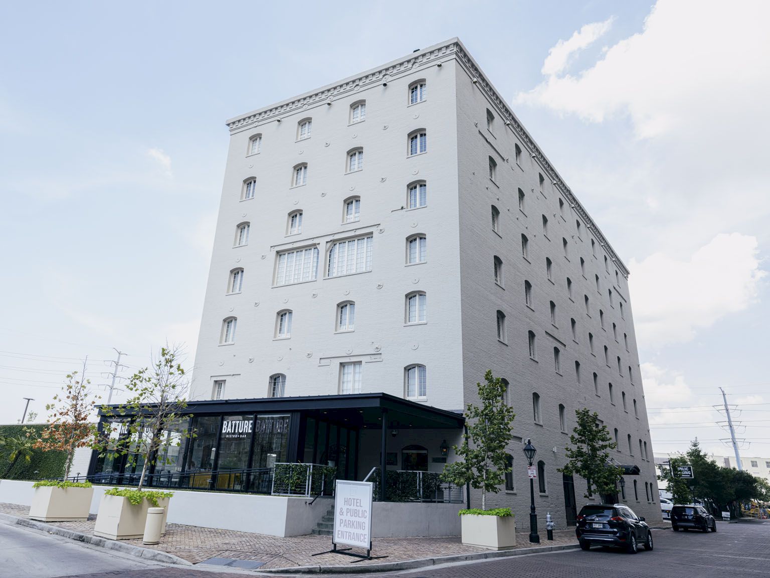 A modern, light-gray, multi-story building with many small windows and a glass-ground-floor entrance; street view with parked cars.